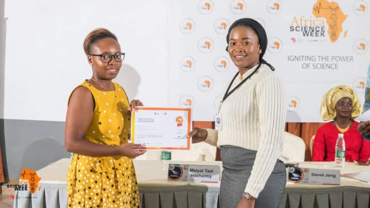 A certificate presentation in front of the event backdrop